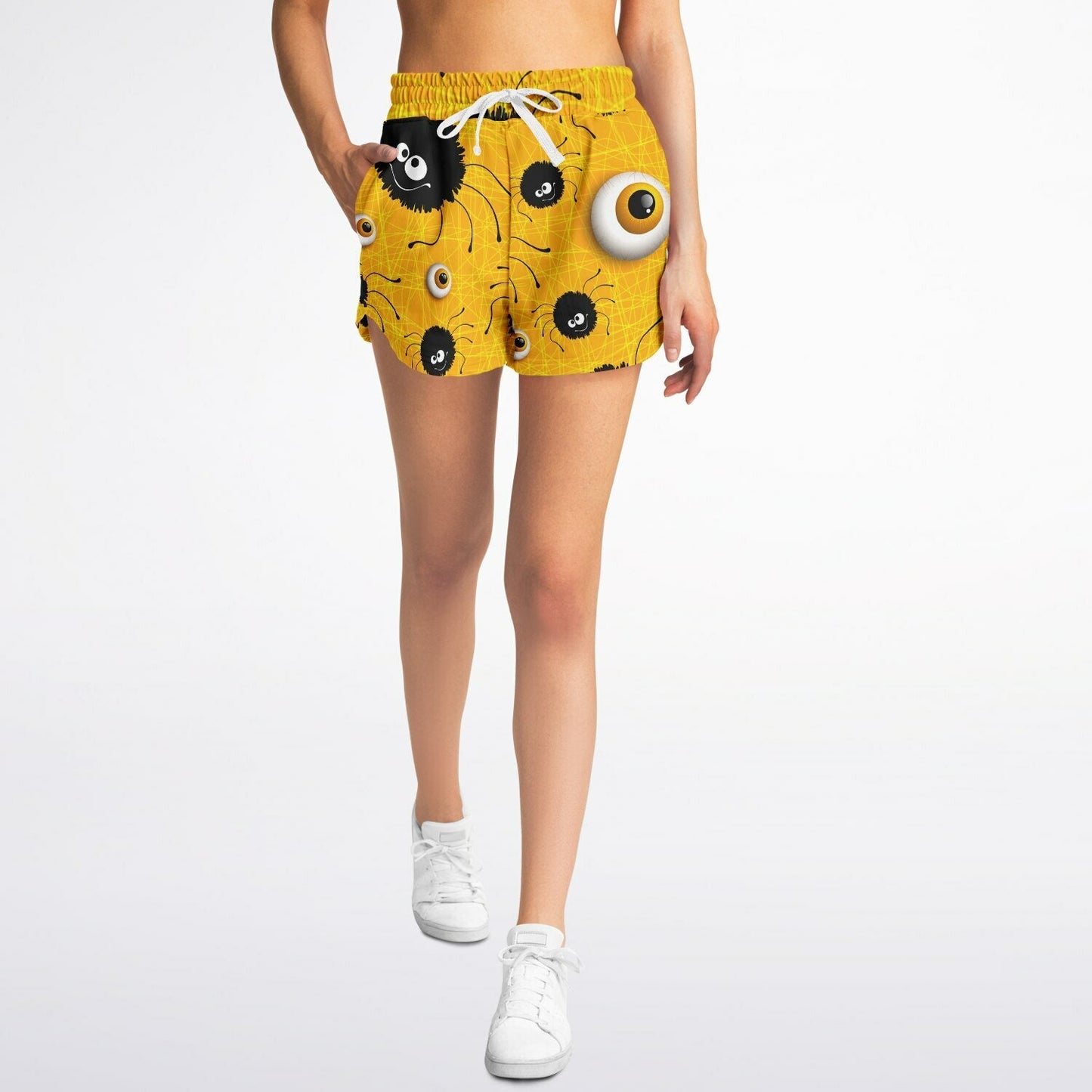 A woman walking, wearing yellow Halloween shorts with a spider and eyeball pattern and white sneakers.
