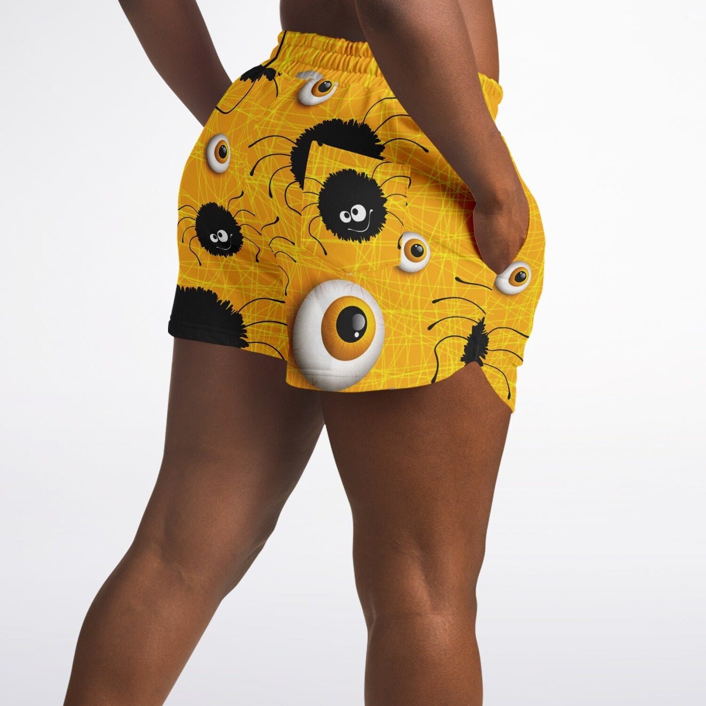 Close-up side view of a woman's hip wearing the yellow spider and eyeball shorts, with a hand in the pocket.