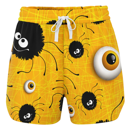 Front view of yellow shorts laid flat, showing a pattern of cartoon spiders and eyeballs with a white drawstring.